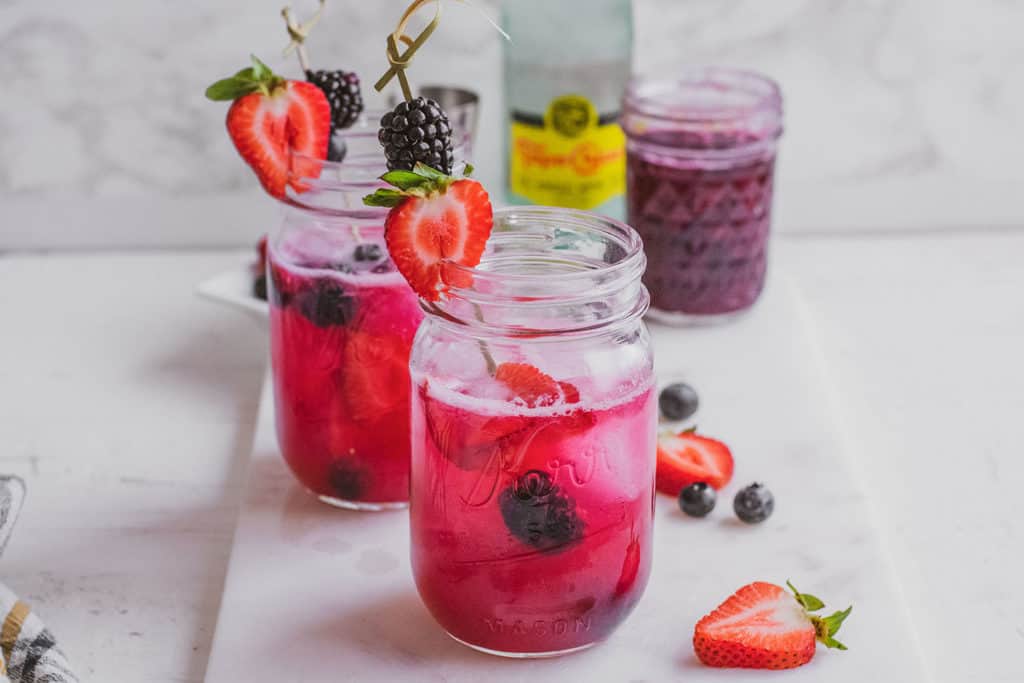 Keto triple berry margarita in a mason jar with strawberries, black berries, blueberries and a topo chico on the side.