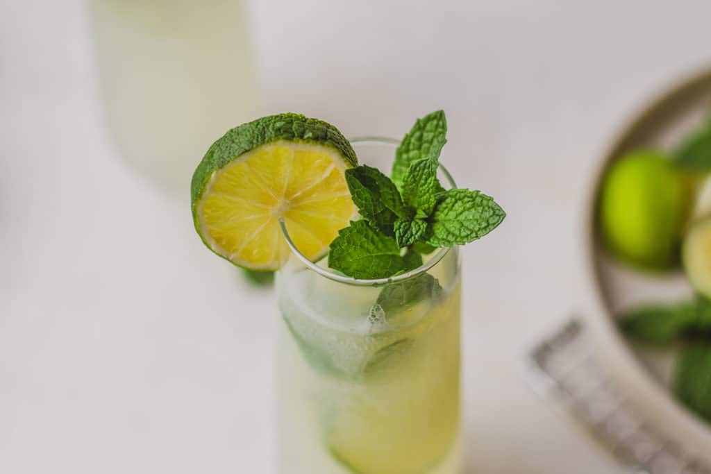 Low carb mojito with limes and mint leaves in a tall clear glass on a white surface. 