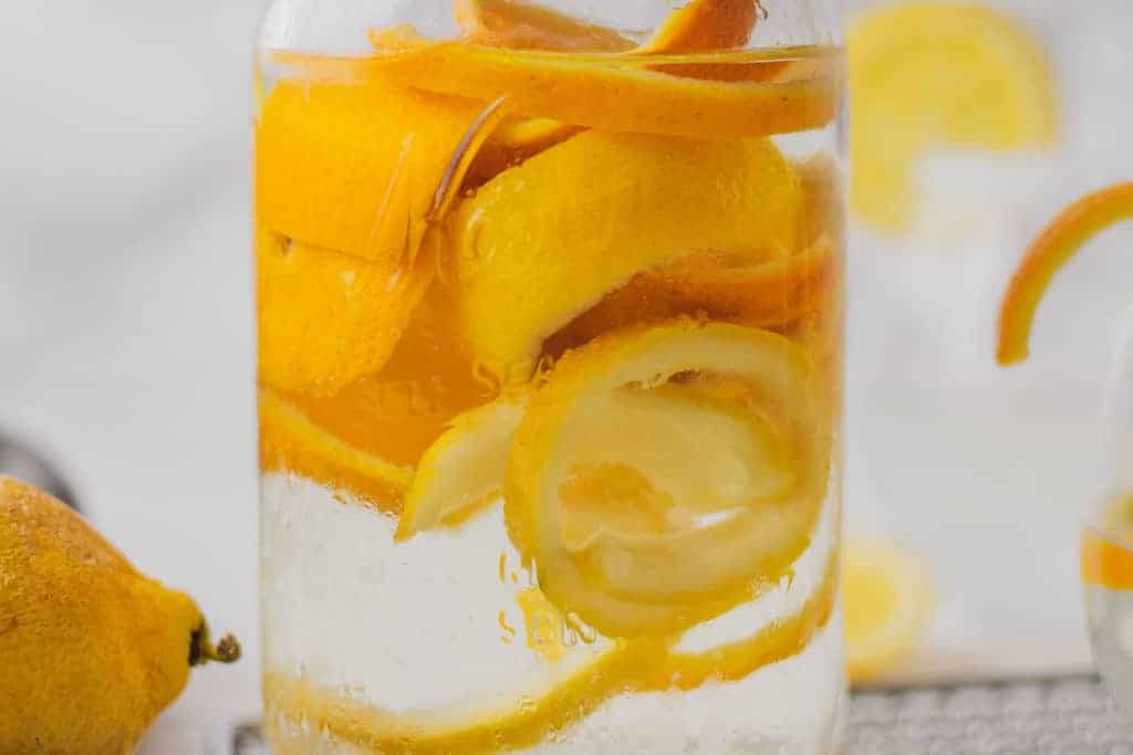 Keto Triple Sec in a mason jar on a white surface with oranges and lemons on the side.