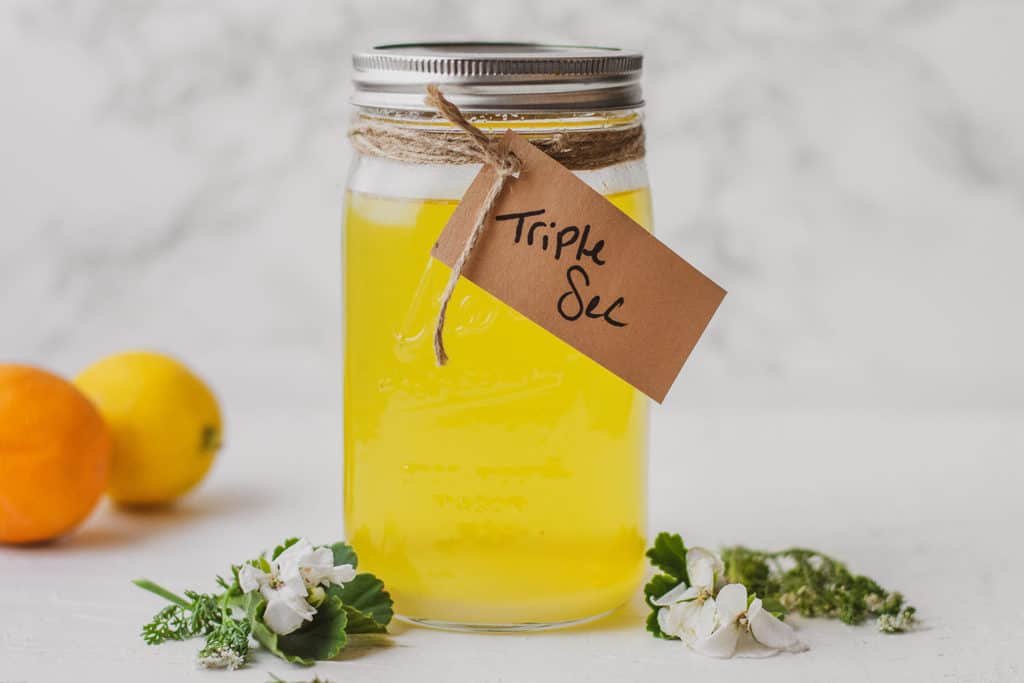 Keto Triple Sec in a mason jar on a white surface with oranges and lemons on the side.
