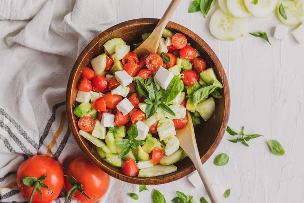 Fresh keto Tomato Cucumber Salad in a wood bowl on a white surface.