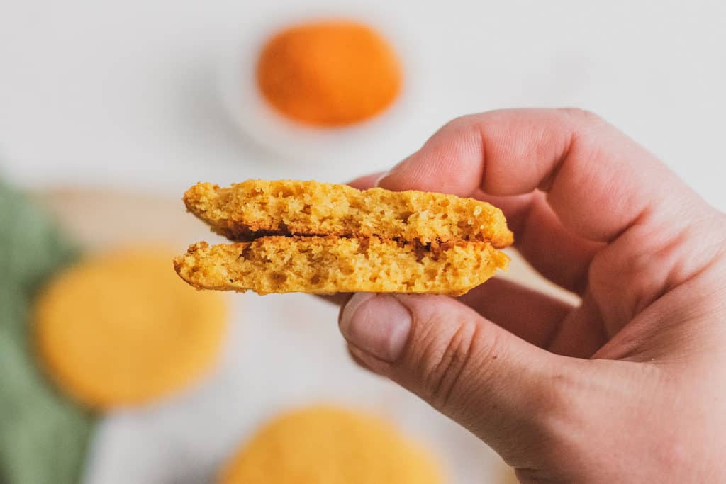 Keto pumpkin cookies held by a hand with ingredients on the side