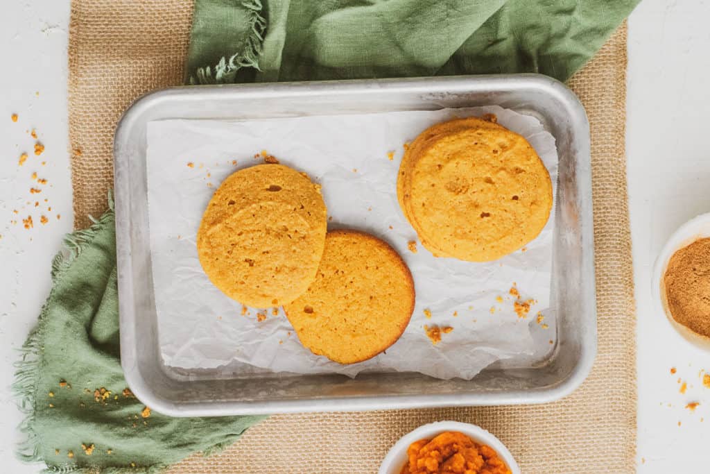 Keto pumpkin cookies on parchment paper with ingredients on the side