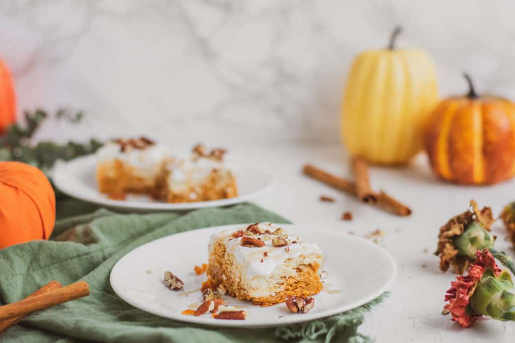 Keto pumpkin cheesecake bars on a white surface with pumpkins in the background.
