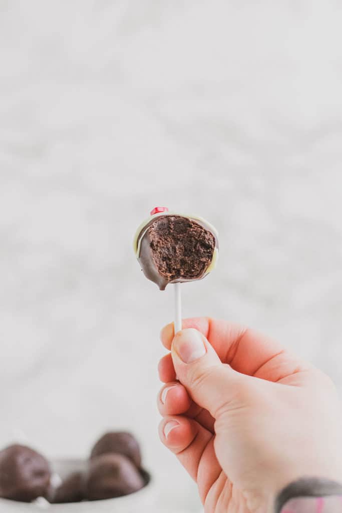 Keto Chocolate Cake Pops with white chocolate drizzle and valentine's day sprinkles on top with a bite taken out and a hand holding it.