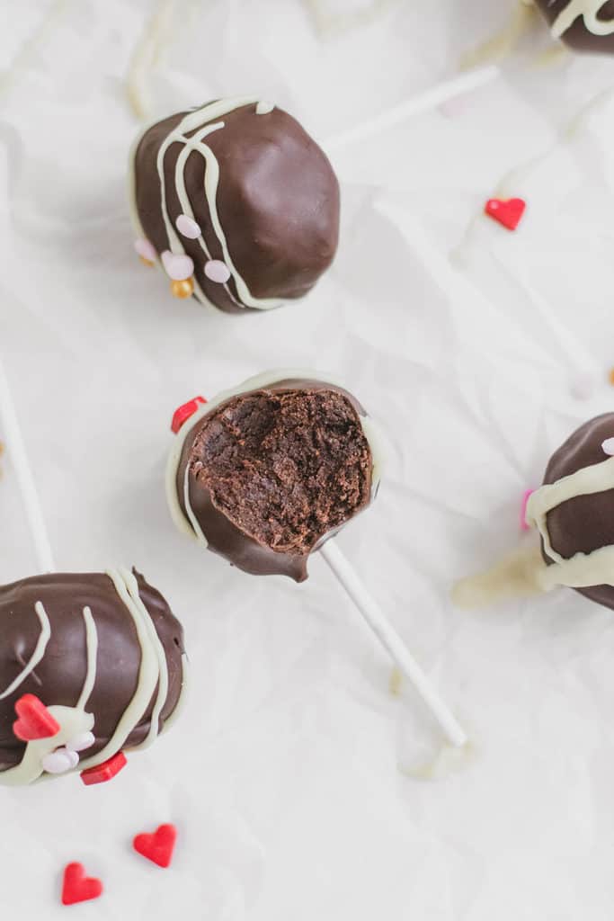 Keto Chocolate Cake Pops with white chocolate drizzle and valentine's day sprinkles on top with a bite taken out.