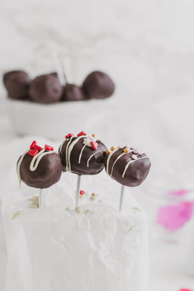 Keto Chocolate Cake Pops with white chocolate drizzle and valentine's day sprinkles on top.