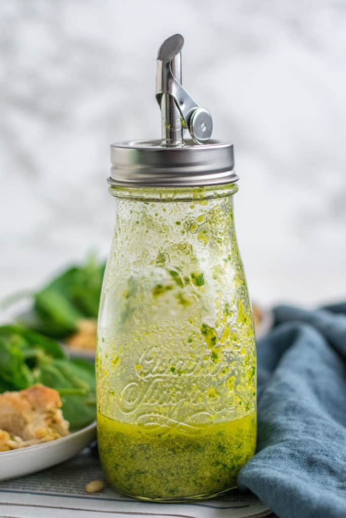 How to Make Basil Pesto recipe in a glass oil jar on a white surface.