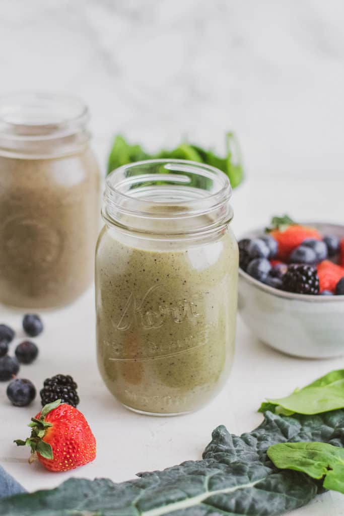 Keto Green Smoothie in a glass jar on a white surface with berries in a bowl in the background. 