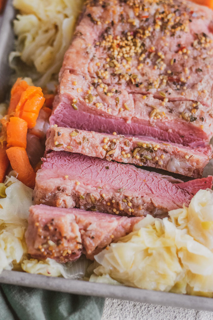 Sliced Keto Corned Beef and Cabbage on a tray with cooked carrots and onions on the side on a white surface