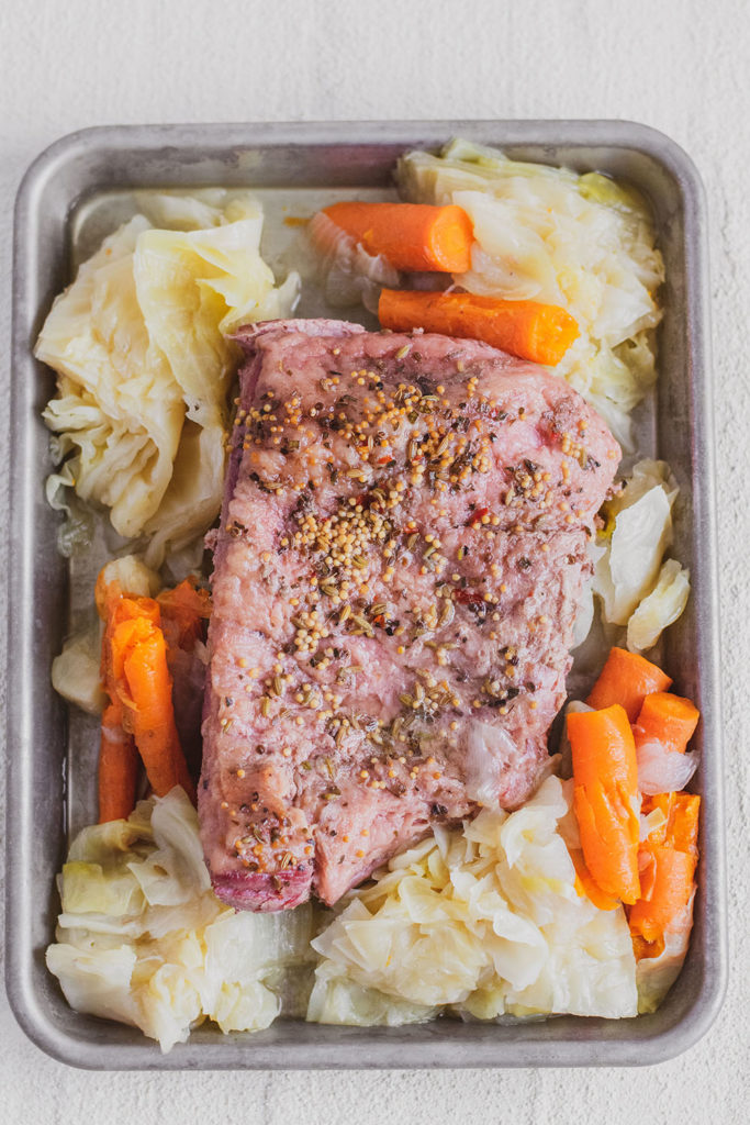 Keto Corned Beef and Cabbage on a tray with cooked carrots and onions on the side on a white surface